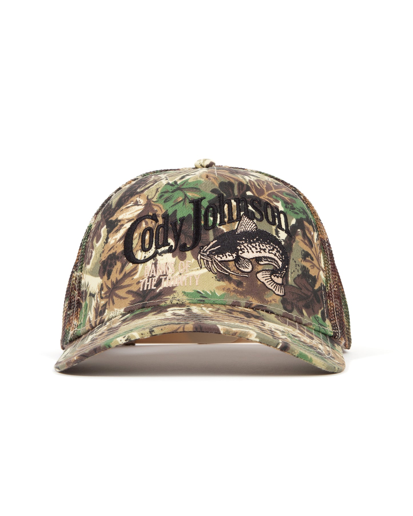 A camouflage trucker cap with a leaf and tree bark pattern. The front features a large black embroidered script reading 'Cody Johnson' above a black catfish graphic.