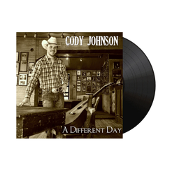 Vinyl record with a cover featuring a man in a cowboy hat and plaid shirt, titled 'A Different Day' by Cody Johnson.
