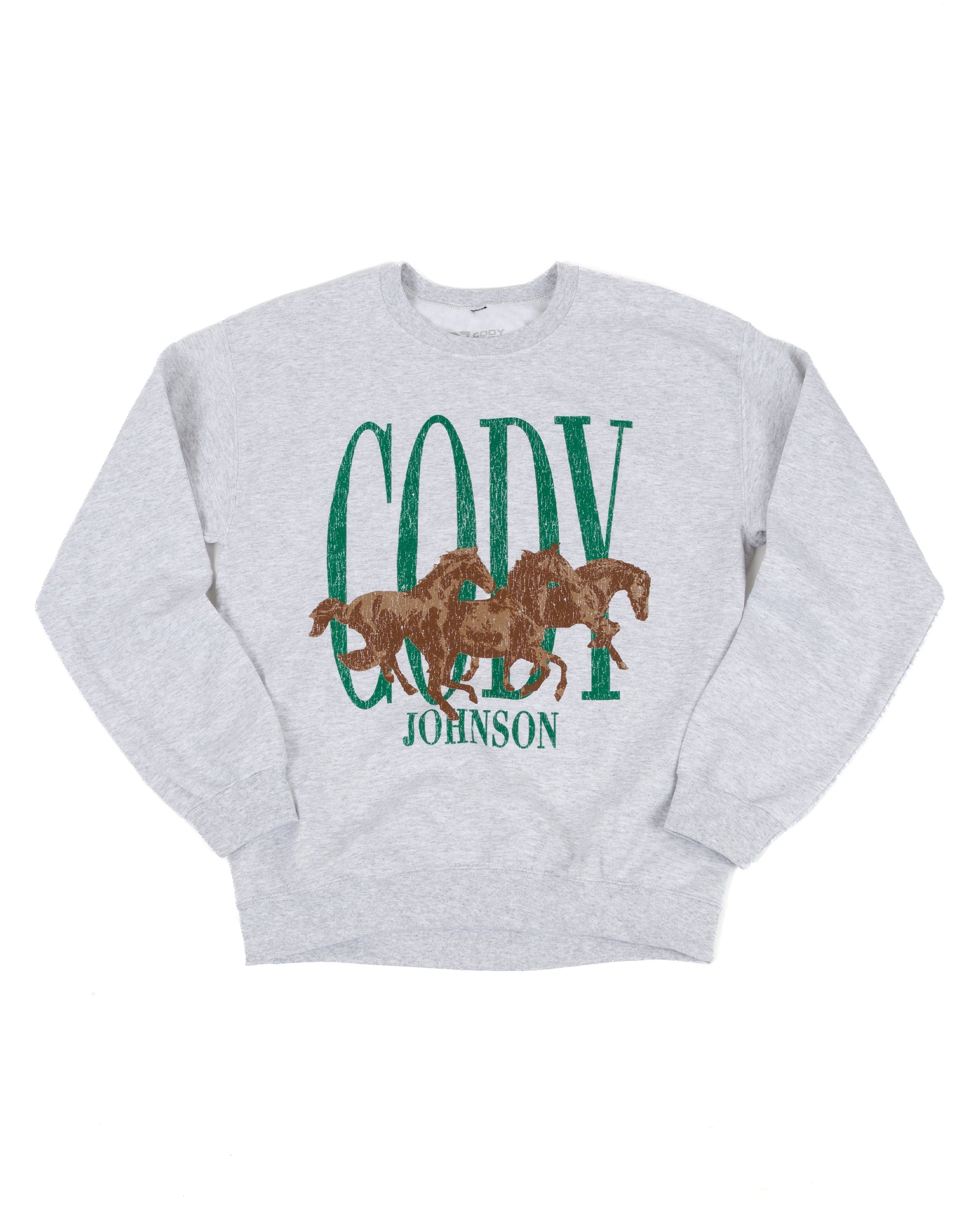 A light heather gray crewneck sweatshirt featuring a graphic print with the word 'CODY' in distressed green letters, three brown horses in the center, and 'JOHNSON' in green text below.
