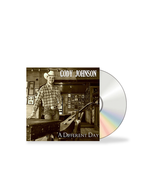 CD cover of 'A Different Day' by Cody Johnson with a person in a plaid shirt and cowboy hat.